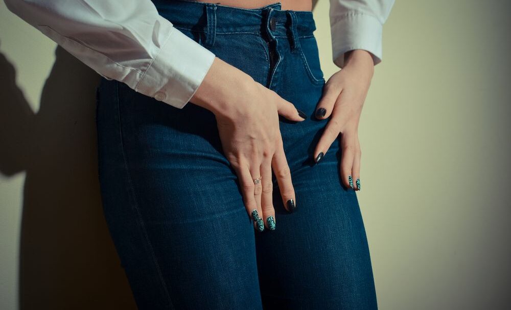 closeup image of pretty female shape with hands on hips wearing jeans long sleeve short & trousers on light copyspace background