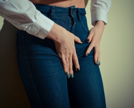 closeup image of pretty female shape with hands on hips wearing jeans long sleeve short & trousers on light copyspace background